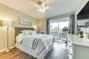 Un dormitorio con cama, mesita de noche, lámpara y vistas al exterior.
