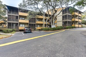 Un edificio de apartamentos de varios pisos con balcones, un estacionamiento y un árbol frente.