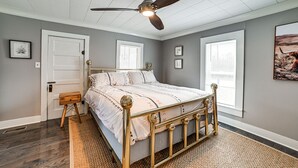 Ein Schlafzimmer mit einem Bett, einem Deckenventilator, einer Tür und Fenstern.