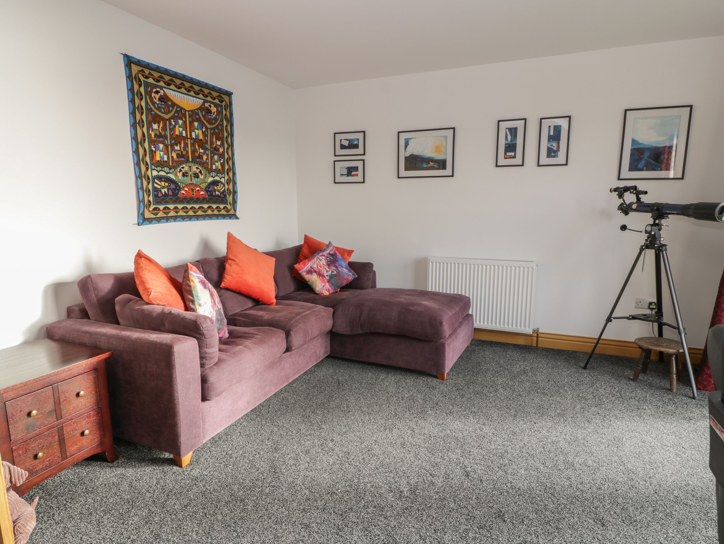 A modern living room with a sectional sofa, a telescope, and framed artwork on the walls.