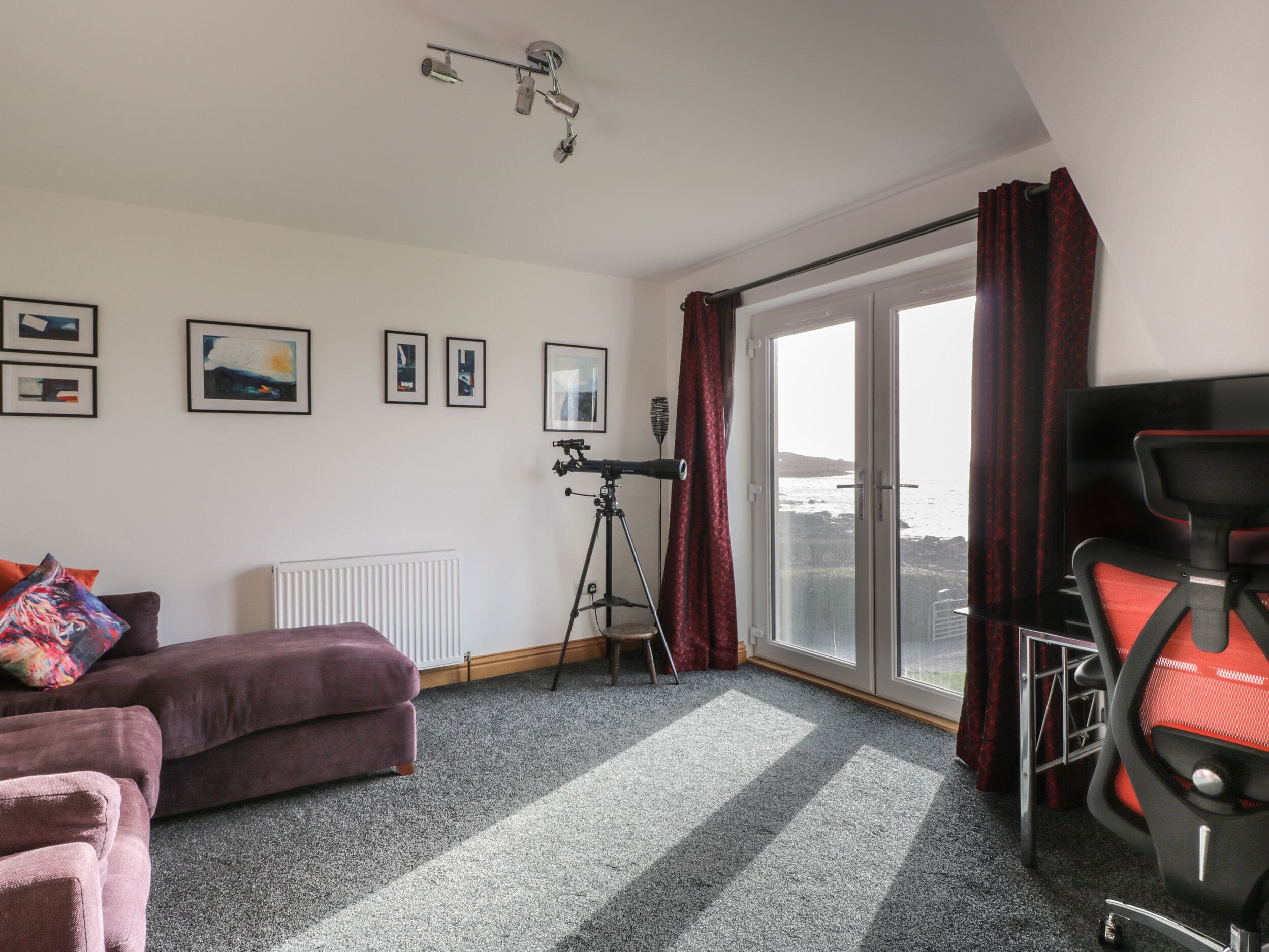 Ein Zimmer mit einem großen Fenster, einem Stativ, einem Sofa und einem Sessel.