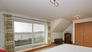 A bedroom with a large bed, a view of the sea, a wooden wardrobe, and a small chest of drawers. - Merse End (Castle Douglas)