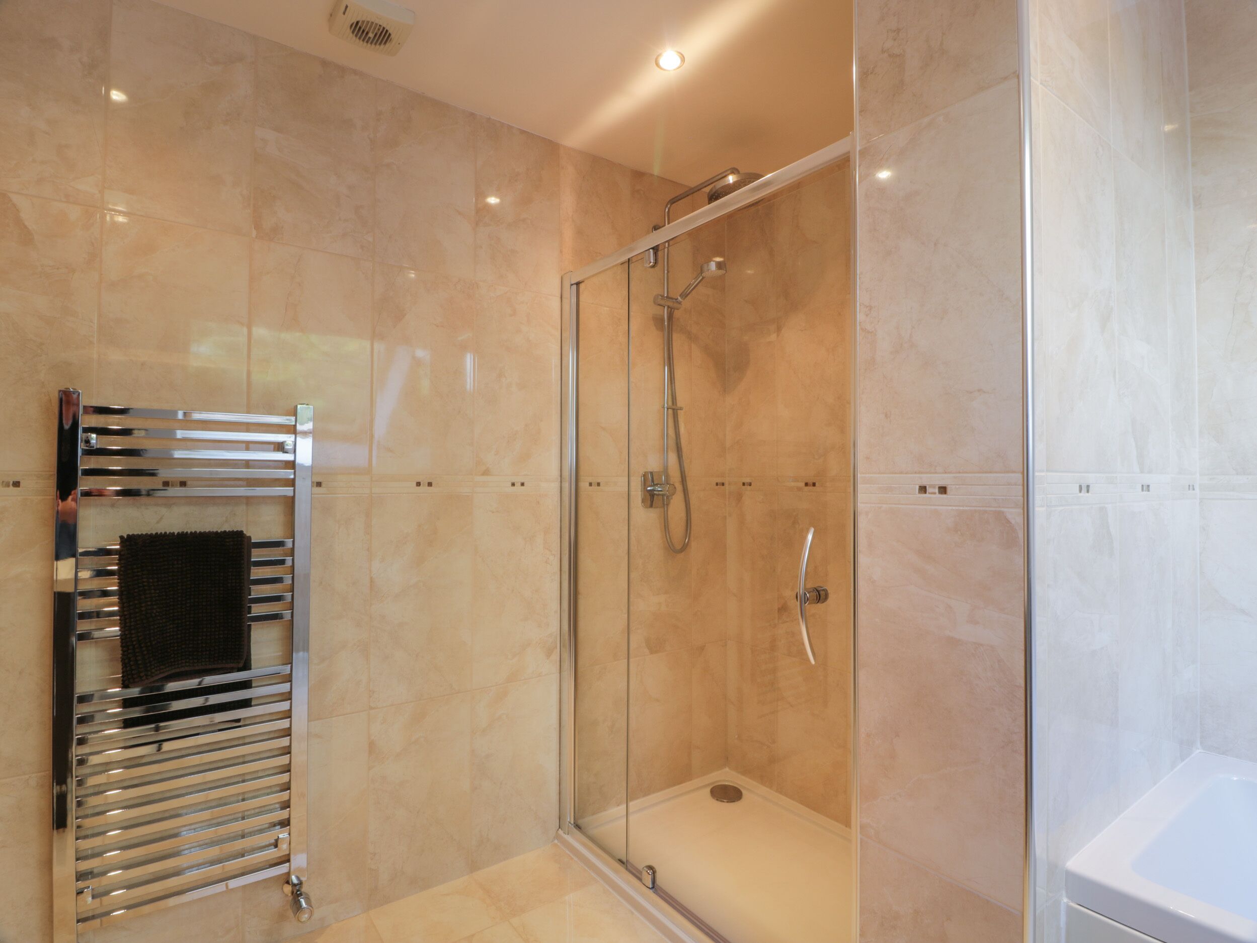Een moderne badkamer met een douchecabine van glas, een ingebouwde handdoekhouder en een losstaand bad.
