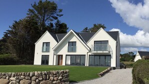 A modern two-story house with a stone wall in the foreground, large windows, and a clear blue sky. - Merse End (Castle Douglas)
