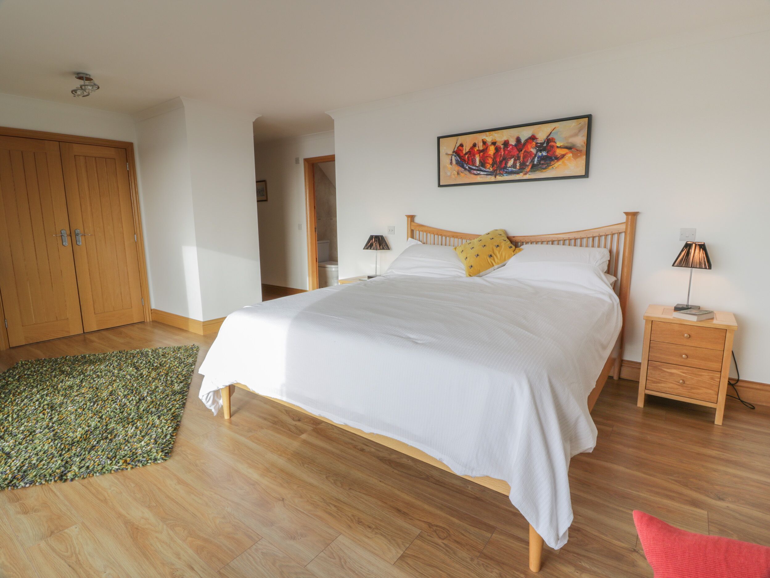 Quarto com cama de madeira, tapete verde, mesa de cabeceira de madeira e um quadro na parede.