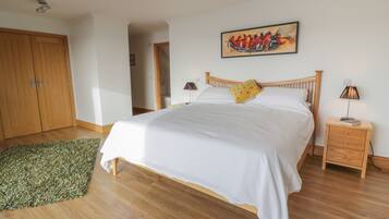 Quarto com cama de madeira, tapete verde, mesa de cabeceira de madeira e um quadro na parede.