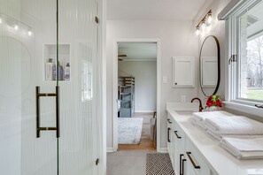 A modern bathroom with a walk-in shower, a vanity with a large mirror, and a window providing a view of the outdoors.