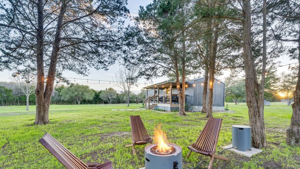 A patio area with a fire pit, outdoor seating, and a building in the background. - Near Majek Vineyard: Private Schulenburg Cabin (Schulenburg)