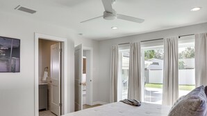 Une chambre dotée d’un grand lit, d’un ventilateur de plafond et offrant une vue sur le jardin arrière grâce à une porte-fenêtre coulissante.