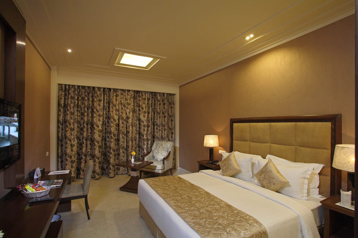 Quarto de hotel com uma cama grande, uma escrivaninha com cadeira, televisão e janela com cortinas.