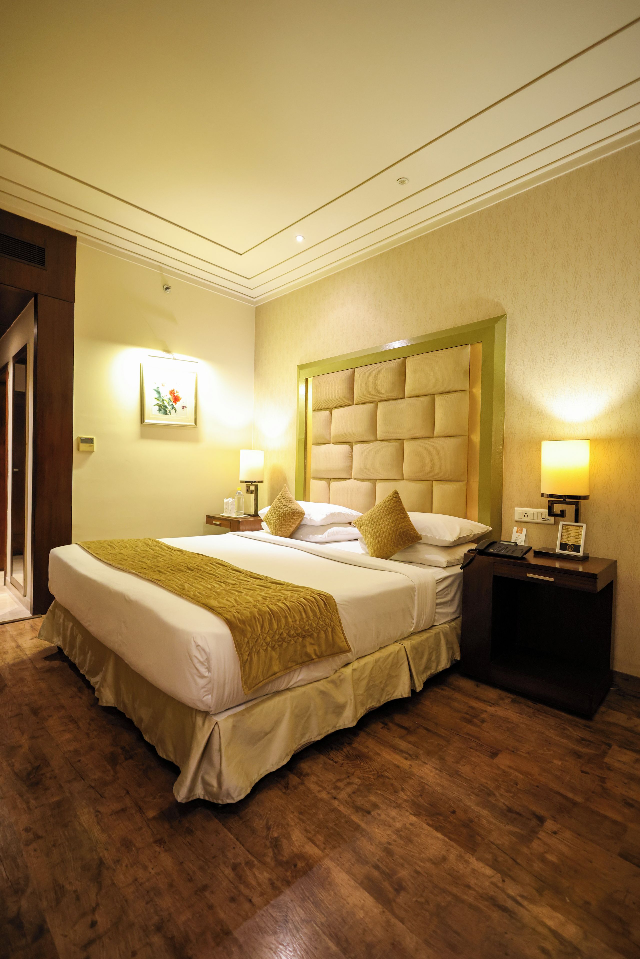A hotel room with a large bed, a nightstand, a bedside table, a wall-mounted lamp, and a framed picture on the wall.