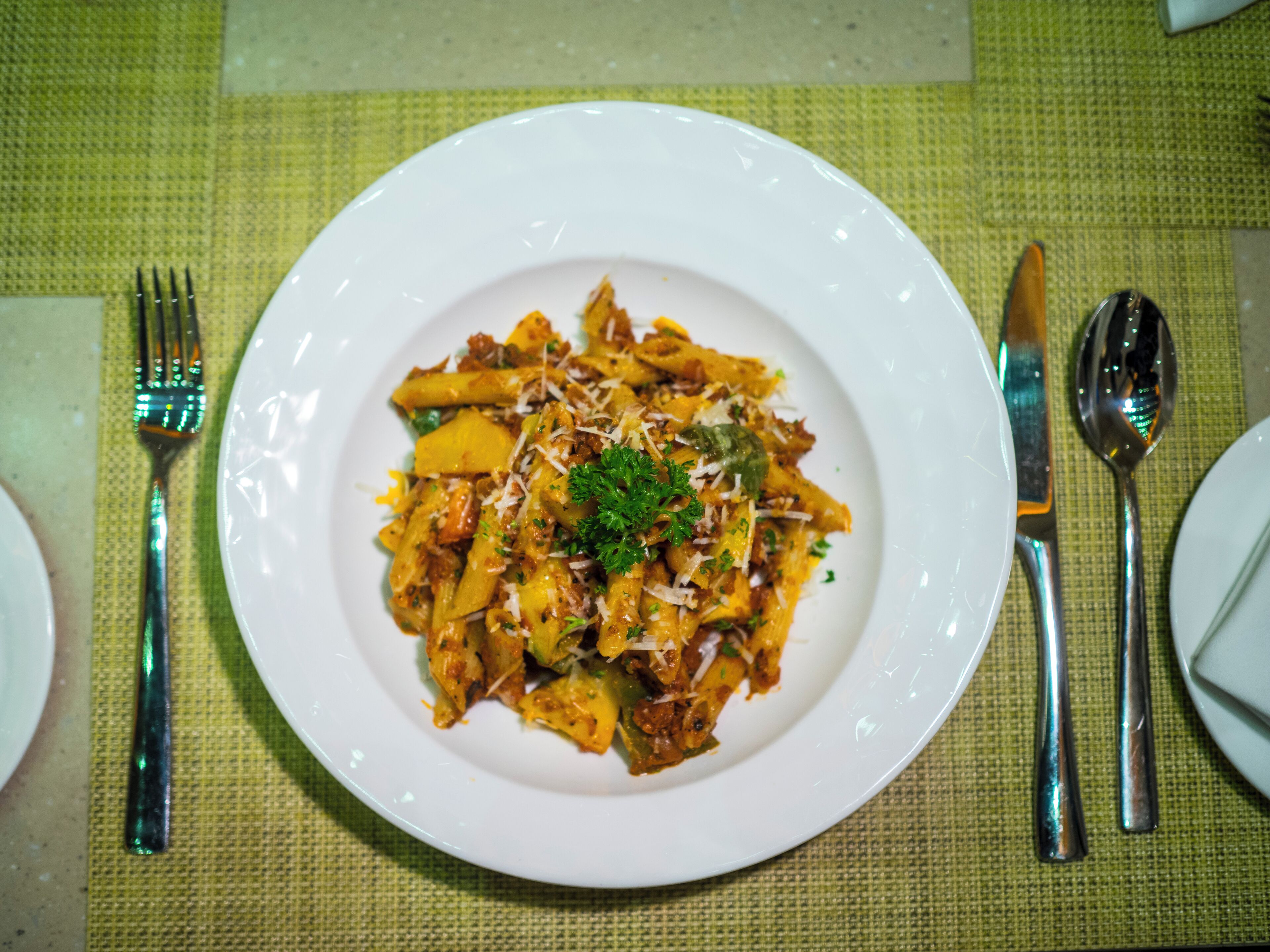 En hvid tallerken med pasta, pyntet med krydderurter, på et bord med en grøn serviet.