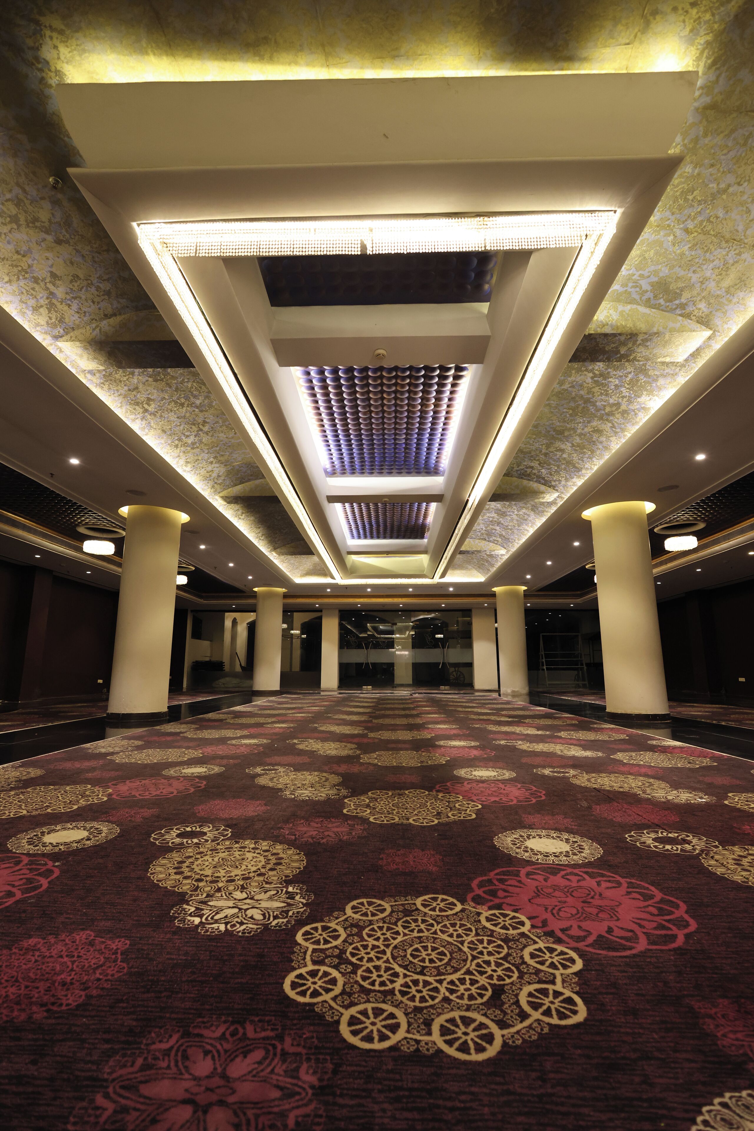 A spacious hall with patterned carpet, large pillars, and a ceiling with recessed lighting.