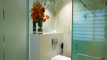 Features a glass shower enclosure, pedestal sink, and a vase with flowers on the countertop.