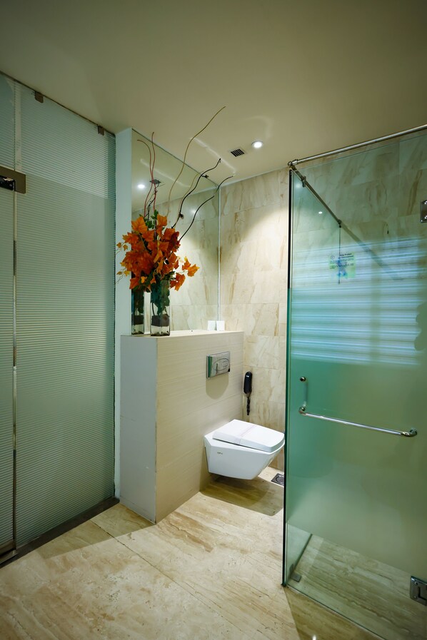 Un baño moderno con cabina de ducha de vidrio, un lavabo blanco y un florero con flores naranjas sobre una estantería.