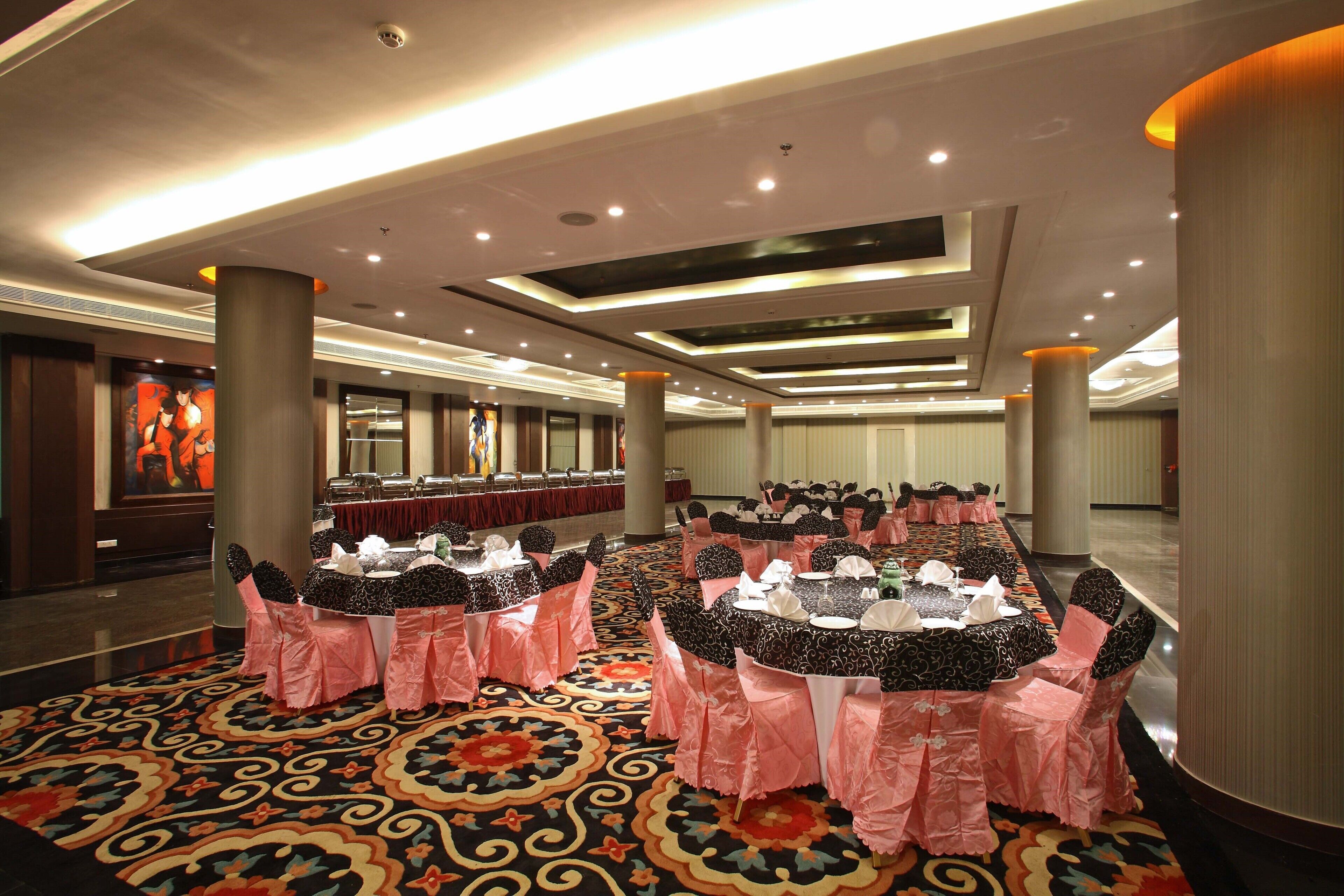 A banquet hall with round tables covered in black and white tablecloths, pink chair covers, and a patterned carpet.