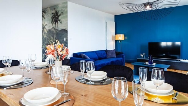A dining area with a wooden table set for a meal, a blue sofa, and a TV in the background.