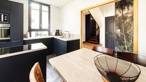 A modern kitchen with dark cabinetry, a large island, and a dining area with a wooden table and a wire chair.