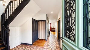 A hallway with patterned flooring, a staircase with black balusters, and a green door with ornate metalwork.