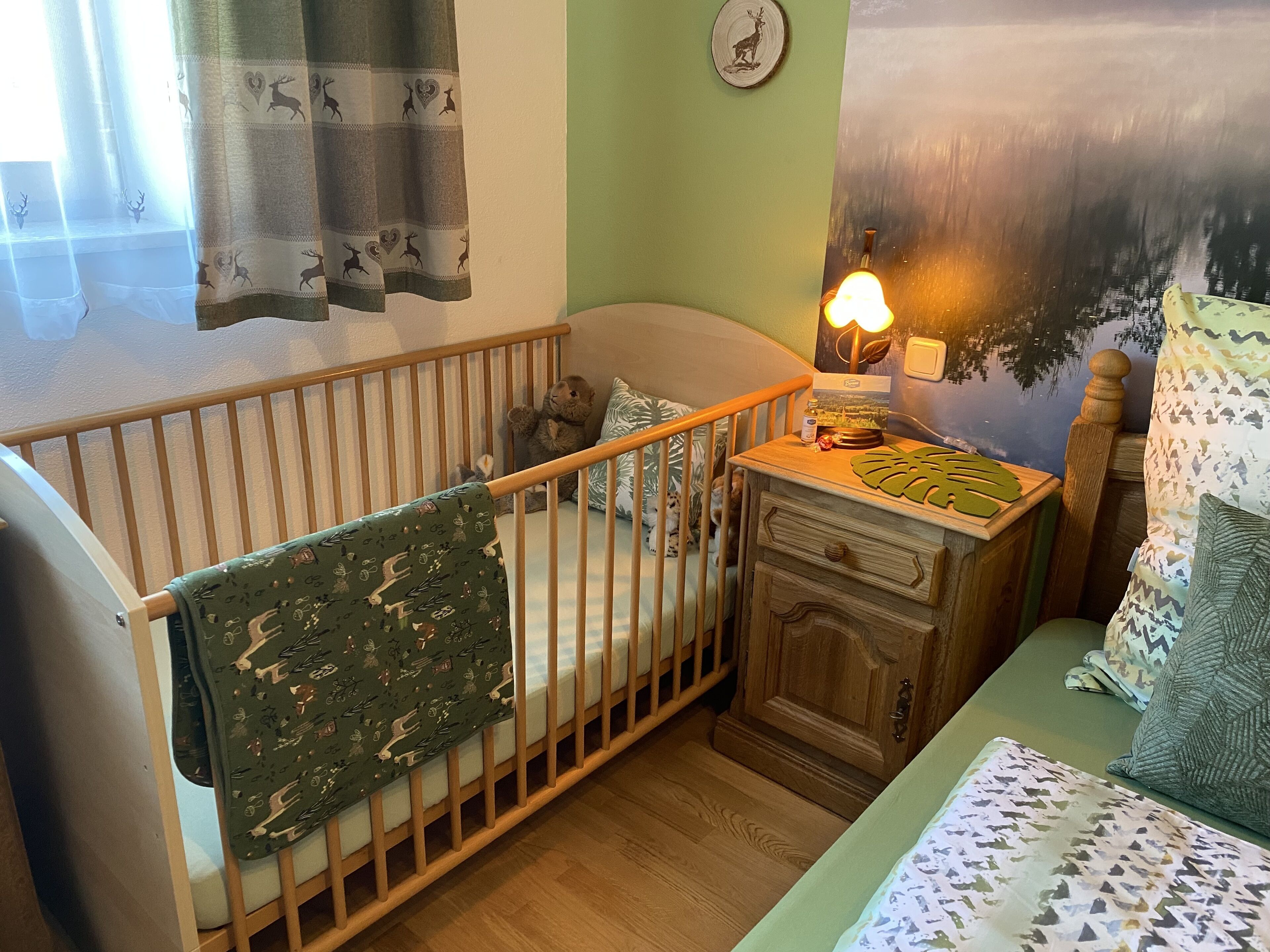 Una habitación acogedora con una cuna, una mesita de noche de madera y una cama con ropa de cama estampada.