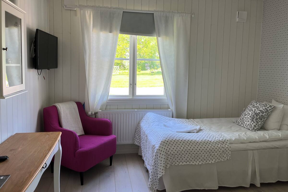 A room with a bed, a chair, a table, and a window with curtains.