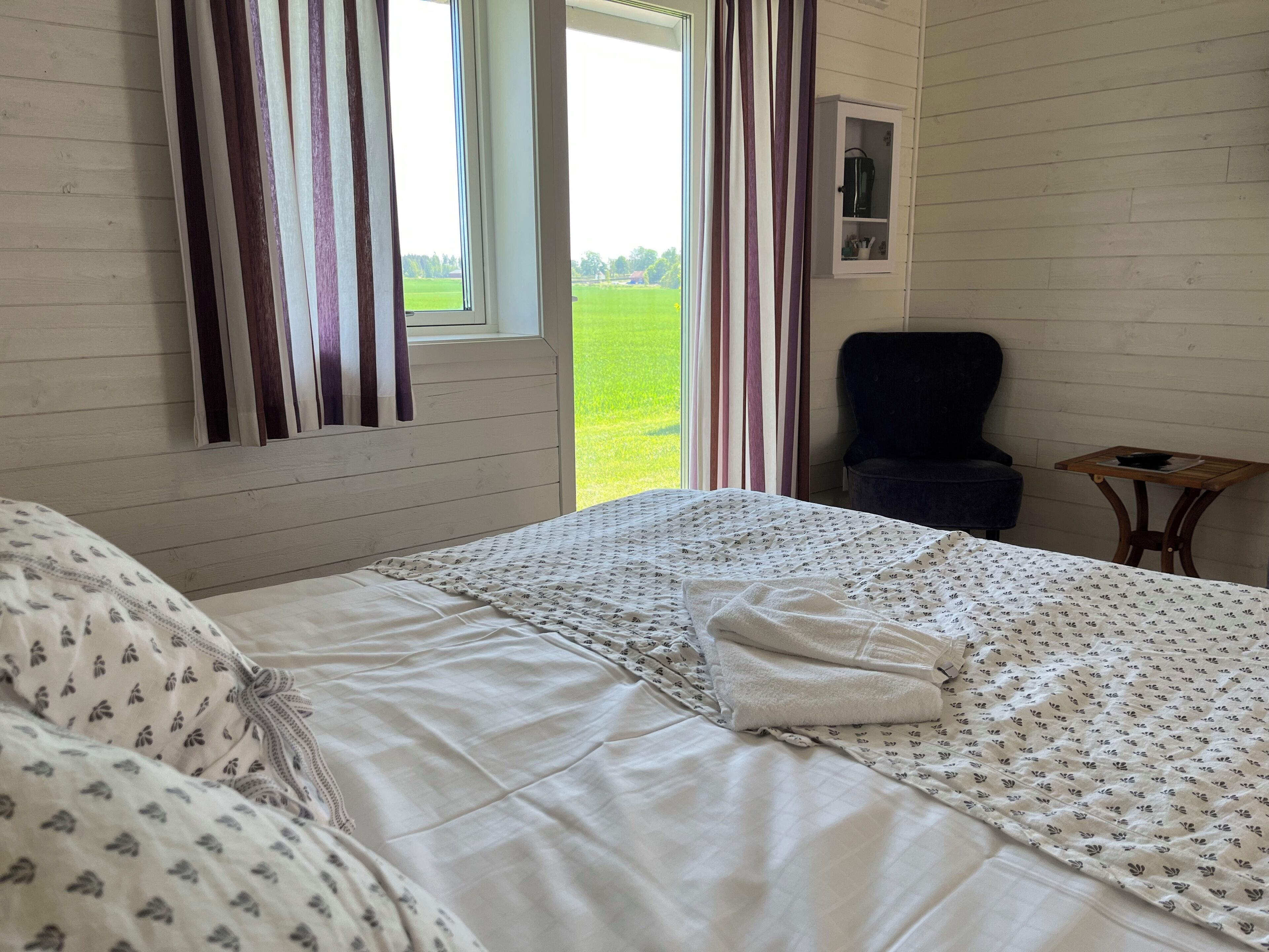 A bedroom with a large bed, a chair, a small table, and a window with curtains.