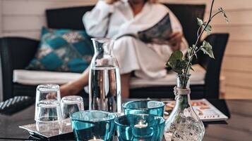 Ett rum med en soffa, ett glasbord med ljus, en vas med en växt och en person som läser en bok.
