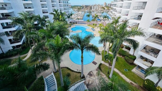 A resort with multiple white buildings, a central swimming pool, and palm trees. - Beautiful in marina, amazing views by Gpsrentas (Mazatlán)