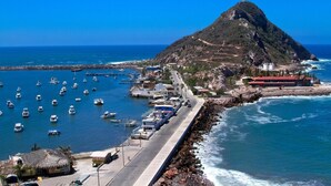 A coastal town with a prominent hill, a marina with numerous boats, and a road leading to a building with a red roof. - Beautiful in marina, amazing views by Gpsrentas (Mazatlán)