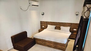 A bedroom with a wooden bed, a brown sofa, and a small wooden table. - Vrindavan Resort (Mathura)