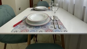 A dining table set with plates, cutlery, and a wine glass, surrounded by chairs and a patterned table runner. - Peace Apartments (Durrës)