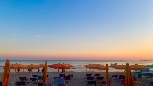 A beach with rows of sun loungers and umbrellas, a calm sea, and a clear sky. - Peace Apartments (Durrës)