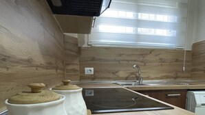 A kitchen with wooden cabinets, a stainless steel sink, and a black countertop. - Peace Apartments (Durrës)