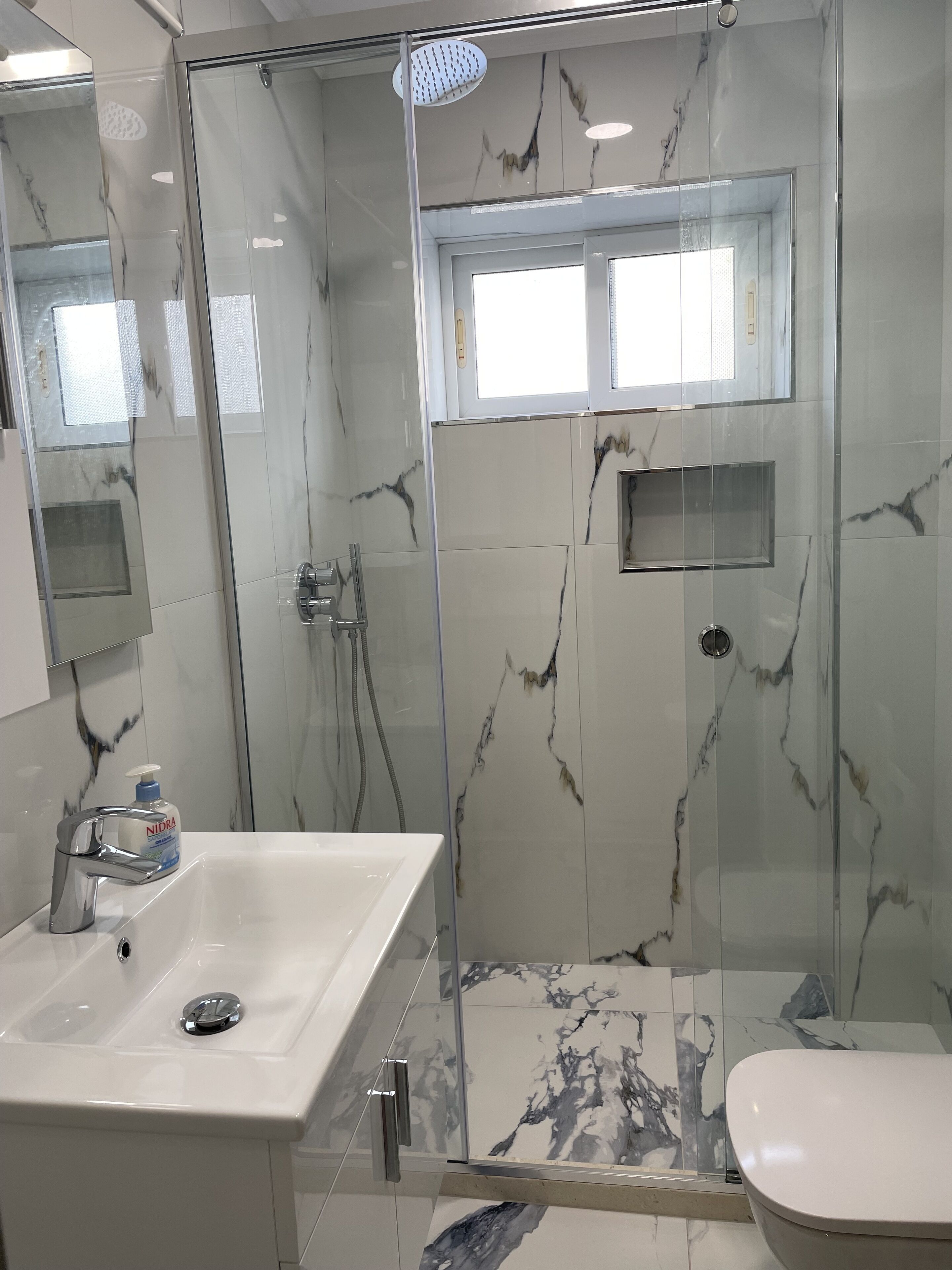 Et moderne badeværelse med et glasafskærmet brusebad, en vask med sæbedispenser og et toilet.