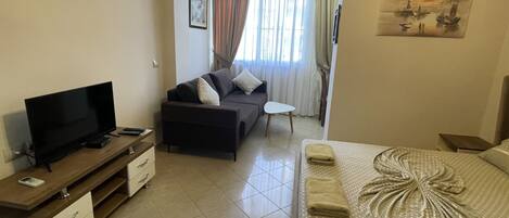 A hotel room with a bed, a TV, a sofa, and a small table.