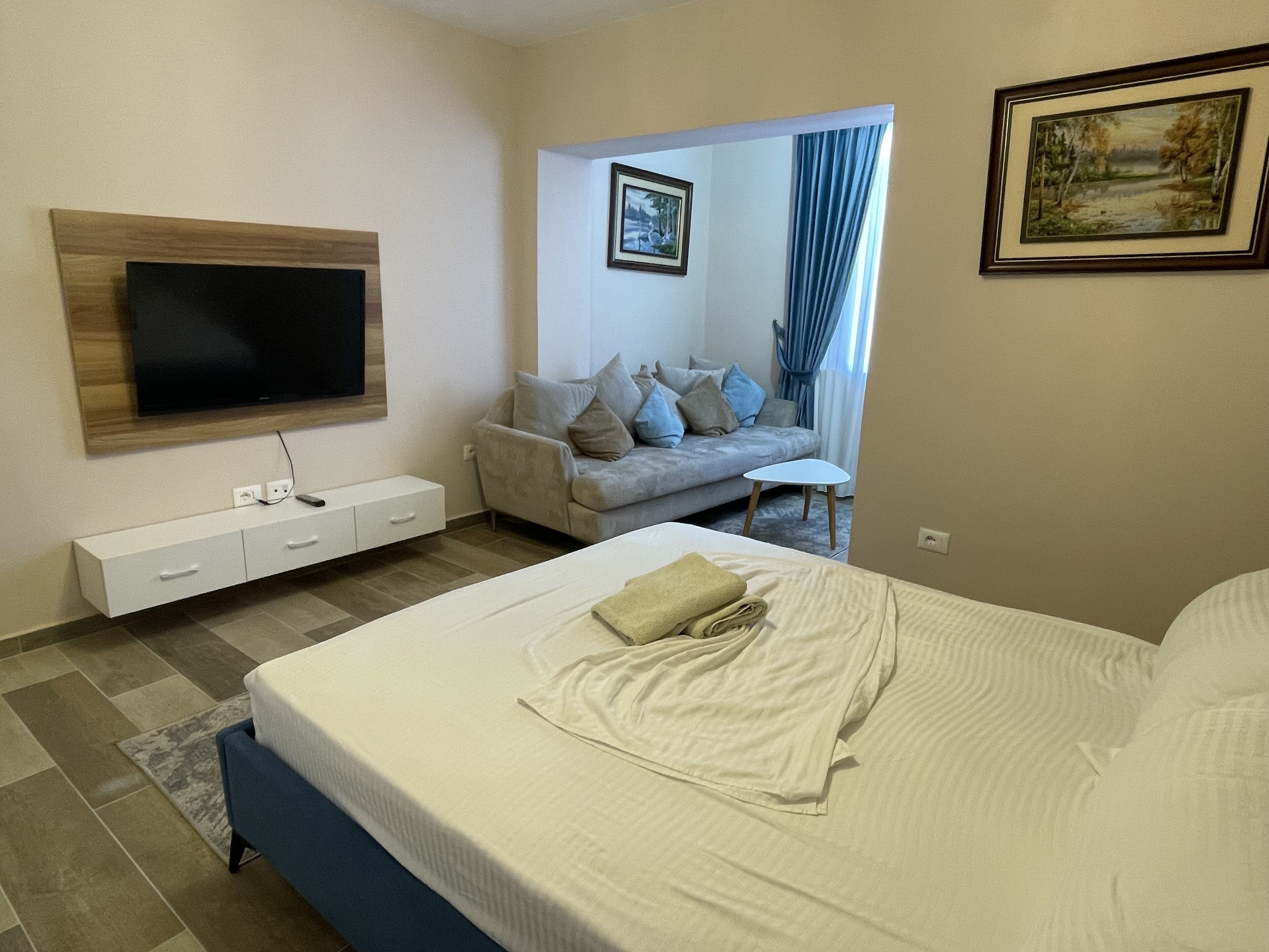 A modern hotel room with a large bed, a flat-screen TV mounted on the wall, a sofa, and a small table.