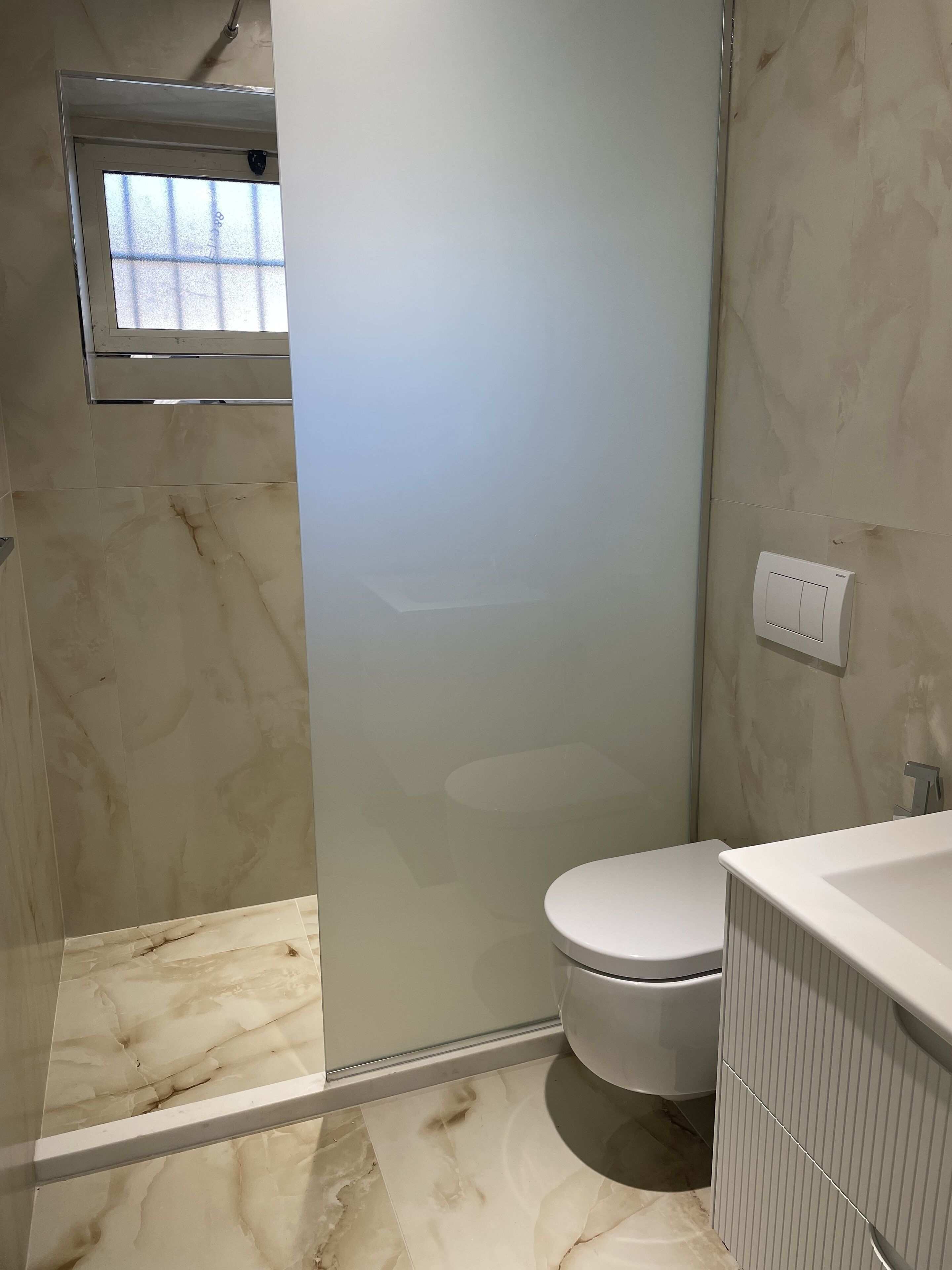 A bathroom with a toilet, a shower, and a small window.