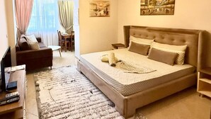 A bedroom with a large bed, a sofa, a desk, and a television. - Peace Apartments (Durrës)