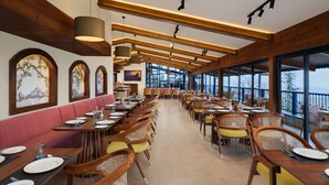 Un restaurante con vigas de madera, amplios ventanales y una larga zona de comedor con mesas y sillas.