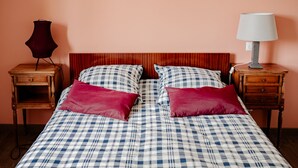 Ein Bett mit kariertem Überwurf und zwei Kissen, das von zwei Nachttischen mit Lampen begleitet wird, in einem Zimmer mit pfirsichfarbenen Wänden.