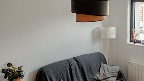 Ein gemütliches Wohnzimmer mit einem dunkelgrauen Sofa, einem runden Holztisch und einem kleinen Beistelltisch mit einer Pflanze.