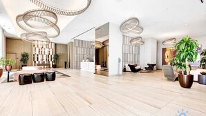 A spacious lobby with a modern design, featuring a central seating area with a table and chairs, a reception desk, and decorative lighting. - Luxury Condo | Stunning View | Resort Amenities (Hollywood)