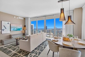 Quarto de hotel moderno com vista para a cidade, área de refeições com mesa redonda e espaço de estar com sofá.