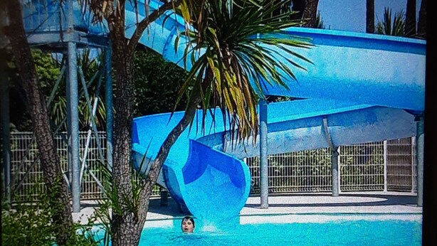 A water slide at a poolside area with a clear sky and palm trees. - Appartement Village de Vacances (Parentis-en-Born)