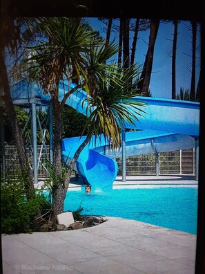 A water slide at a poolside area with a clear sky and palm trees. - Appartement Village de Vacances (Parentis-en-Born)