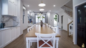 Une cuisine moderne avec des meubles blancs, un pare-feu en marbre et un coin repas comprenant une table en bois et des chaises blanches.