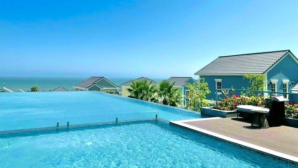 Une piscine avec vue sur l’océan, un patio couvert avec des sièges et un bâtiment à la façade bleue.