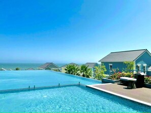 A swimming pool with a view of the ocean, a covered patio with seating, and a building with a blue exterior. - JB. Nguyen Villa NovaWorld Phan Thiet (Phan Thiet)