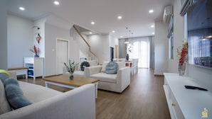 Un salon moderne avec un escalier, un coin repas et une cuisine en arrière-plan.