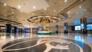 A spacious lobby with a large circular emblem on the floor, a central decorative fountain, and multiple screens displaying content. - MGM Signature | No Resort Fees, Jacuzzi & Pools (Las Vegas)
